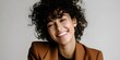 © Berkah - Smiling woman with dark curly hair wearing a brown blazer against a plain background