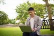 © matinee - Thoughtful young Asian man solving a problem while working on a laptop outdoors.