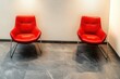 © btiger - Two red modern lounge chairs on gray marble floor against neutral wall in a minimalist waiting area, quiet and calm atmosphere suggesting anticipation
