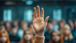 © Mariya - raised hand in a sweater among a blurred attentive audience expressing eager participation and engagement during a lecture or meeting