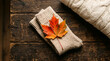 © AsimRazzaq - Autumn still life with a vibrant maple leaf on a folded knitted sock and a cozy sweater on a rustic wooden table.