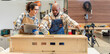 © BESTIMAGE - Two carpenter workers working on project together Black male carpenter wearing safety gloves measuring by measuring tape with female colleague holding digital tablet in woodworking workshop