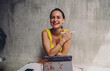 © BullRun - Joyful multiracial female digital artist laughing looking at camera with stylus pen, happy Hispanic creator expressing positive attitude inside cozy productivity biophilic cafe copy space.