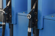 © Paweł Michałowski - Diesel fuel nozzles at station. Black handles rest inside blue pumps. Metal spouts point upward. Diesel labels mark both dispensers. Fuel equipment fills background. Refueling hardware in closeup.