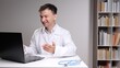© Aliaksandr - Doctor in a white coat smiling and gesturing while having a video call on a laptop, providing remote healthcare services from a home office with a stethoscope on the desk