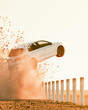 © Nusaba - White Race Car Airborne Moment: A sleek white race car soars through the air, kicking up a cloud of dust as it clears a row of short fence posts against a backdrop of warm, hazy sunlight.