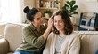 © Robson - Woman with hair bun sits on a sofa, gently touching her friend's wavy brown hair in a bright room with plants. friendship, care, lifestyle, home, indo