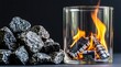 © miss irine - Fire burns in glass cylinder with charcoal logs inside. Pile of rough grey rocks sits beside object. Dark background creates contrast, highlights glowing flames and warm light.
