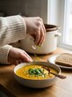 © SITI - Person Garnish Fresh Green Parsley on Hot Lentil Vegetable Soup Bowl in Cozy Bright Home Kitchen