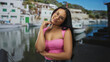 © Krakenimages.com - Young latin woman wearing glasses, hand to chin gesture, pink top, posed before a marina scene in a studio; contemplation.