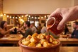© mtmakos - A hand pouring spicy brava red sauce over crispy fried potato cubes in a terracotta dish, set against the blurred background of a lively traditional tapas bar.