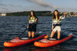 © Roman - Two women paddleboarding on calm lake water