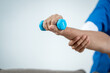 © Thitaporn - Close-up of a person holding a blue dumbbell while another person supports the forearm during arm exercise or rehabilitation.