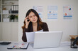 © wattana - Young Asian businesswoman discussing work by phone at her office desk.