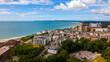 © Amazing Aerial - Aerial view of the Bournemouth coastline featuring the sandy beach, urban architecture, and lush greenery under a bright blue sky, Bournemouth, England, United Kingdom.