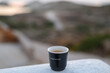 © Mat Hayward - A black espresso cup rests on a white ledge overlooking a blurred rocky landscape, capturing a peaceful moment of coffee enjoyment in natural light.
