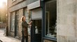 © SashaMagic - Store owner closing shop with roller shutter in late afternoon light, urban street scene with copy space