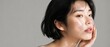 © Dzianis - Close up beauty portrait of a young woman touching her cheek with smooth glowing skin against a neutral gray background with copy space