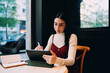 © BullRun - profile view of young woman writing with smart stylus on digital tablet screen inside cafe, female student taking online notes from open notebook during distance e-learning course