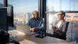 © CarlosBarquero - Business professionals collaborating at shared workspace, using laptops and discussing strategy with cityscape visible through large windows