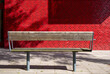 © ankihoglund - Empty wooden bench with red tile wall in the background.