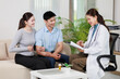 © Tj - Young Asian couple sitting on a couch, consulting with a smiling female doctor reviewing medical documents and offering healthcare guidance in a professional office