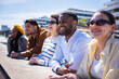 © CarlosBarquero - Group of multicultural friends enjoy a bright sunny day while leaning on a ledge in a contemporary residential neighborhood with modern architecture.