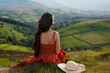 © Iryna - Woman sitting on a hilltop looking at green fields on a sunny day in the countryside