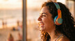 © ryker - Young woman laughing wearing colorful headphones enjoying music at sunset with curly hair and warm light