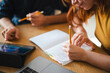 © Studio Marmellata - A man and a woman work together at a table. The woman writes in a notebook while the man looks at a tablet during their collaborative project session in an office.