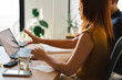 © Studio Marmellata - A woman with auburn hair sits at a desk while holding a small card and gesturing toward a laptop screen. She is collaborating with a colleague in a home office.