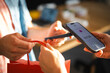 © Studio Marmellata - A customer uses a smartphone for a contactless payment at a store. The cashier hands over a red shopping bag as the transaction completes in the retail shop.