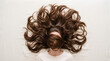 © Emre Akkoyun - Woman lying on white bed, long brown wavy hair surrounding her head, focusing on hair care and natural beauty