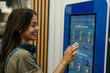 © La Famiglia - Woman smiling using self-service laundromat touch screen terminal