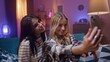 © VAKSMANV - Two joyfull young girls are posing to smartphone. Friends are taking selfie and smiling. Younf women are making post for social network. Best friends sitting on couch and having fun.