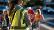 © Kateryna - Rear view of school crossing guard holding a stop sign helping elementary students cross a bright street safely near the school building during the morning commute safety concept outdoor