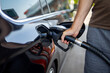 © Iryna - Person Refueling Black Car at Gas Station. Close-up of a person holding a fuel pump nozzle inserted into the open filler neck of a glossy black car at a gas station.
