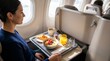 © SashaMagic - Woman enjoys airplane breakfast with yogurt, muesli, and juice in bright cabin light, wide-angle view