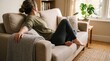© hadz - Partial body view of a young woman relaxing on a comfortable sofa in a bright living room, perfect for wellness websites, mental health articles, and lifestyle branding