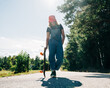 © Cavan Images - Woman in overalls walks with skateboard on sunny road