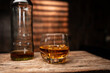 © aekachai - Glass of Whiskey with Ice and Glass Bottle on Rustic Wooden Table in Cellar
