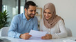 © siraphol - Arab couple smiling while reviewing document in bright office setting
