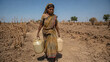© Fiandesain - A woman walks through a dry, barren field carrying two water containers, symbolizing drought and water scarcity
