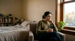 © Zohaib - Thoughtful woman holding a mug sitting in an armchair by the bedroom window