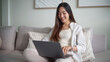 © matinee - Asian woman working online with a laptop while planning her trip at home.