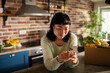 © Davor - Woman using smartphone in home kitchen with fresh groceries
