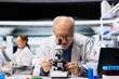 © DC Studio - Senior molecular biologist inspects a new drug compound under a microscope for consistency; elderly man in the research facility verifies medication quality and purity standards during analysis.
