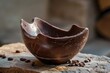 © juliars - Chocolate easter egg broken open, revealing its hollow interior, resting on a rustic wooden surface alongside cocoa beans