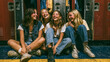 © RB - Four happy young female students sitting together laughing inside school locker hallway wearing casual denim outfits