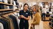 © Akils - Retail associate assists customer with clothing selection using digital handheld device store setting.